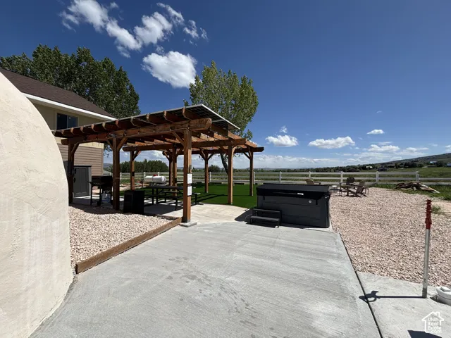 Outdoor space featuring a concrete patio, a wooden pergola with integrated solar panels, artificial turf, a permanent hot tub, and gravel landscaping
