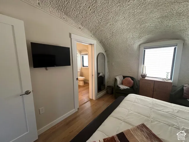 Vaulted textured ceiling, wood-finish flooring, and crisp door trim featuring substantial window casing