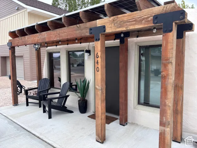Covered entry featuring a rustic timber pergola, heavy-duty black metal corner brackets, integrated roof-mounted solar panels, and a smooth-finish exterior wall
