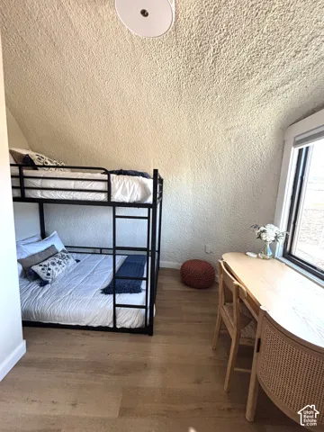Room featuring wood-finish flooring, vaulted textured ceiling, and a large window