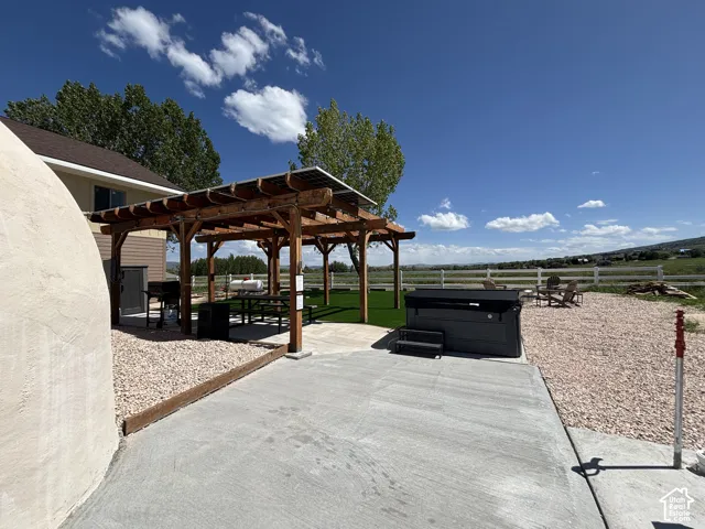 Outdoor recreation area featuring a timber-frame pergola, synthetic turf surfacing, a concrete patio, gravel landscaping, and a built-in spa