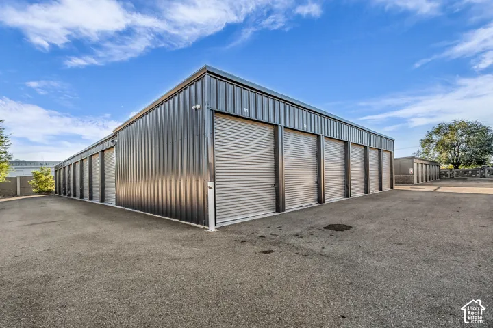 Metal-paneled exterior building featuring multiple roll-up garage doors, a shed-style roofline, and expansive paved surface area