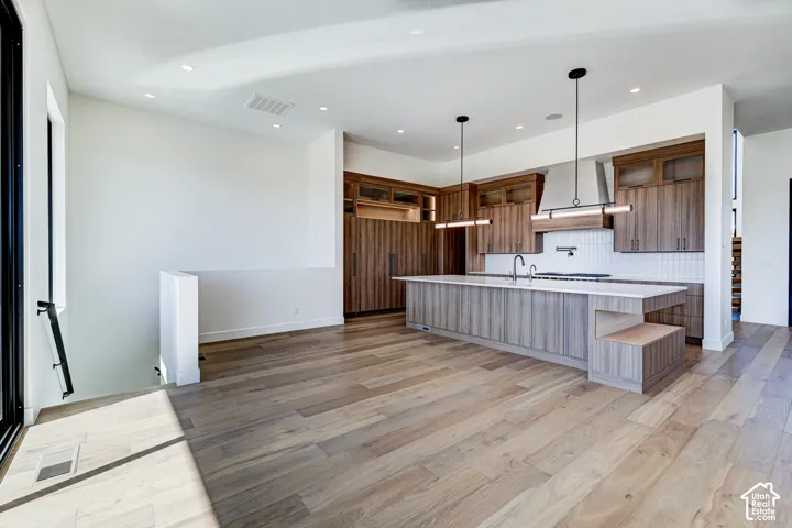 Kitchen featuring wood-finish cabinetry, an expansive center island with a stone countertop, built-in stainless steel appliances, modern pendant lighting, and wide-plank wood-finish flooring