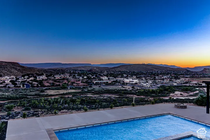 In-ground swimming pool featuring a concrete surround and a stone-encased fire pit, set against a expansive desert mountain and city landscape
