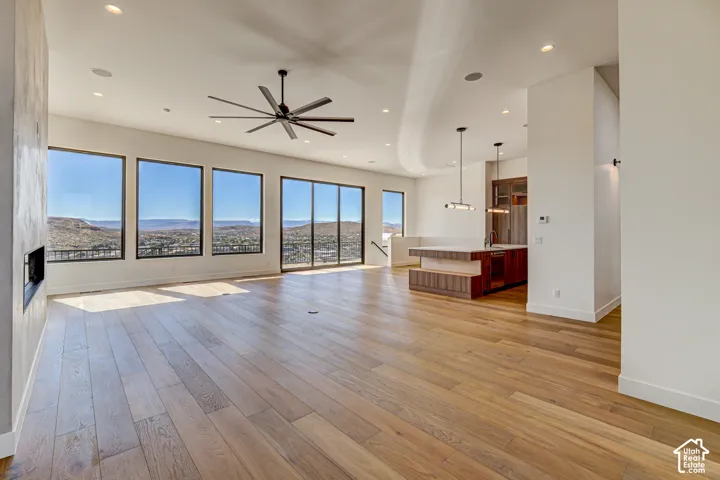 Open-concept interior featuring hardwood flooring, floor-to-ceiling windows with mountain scenery, a recessed fireplace, ceiling-mounted paddle fan, and kitchen island with custom integrated cabinetry