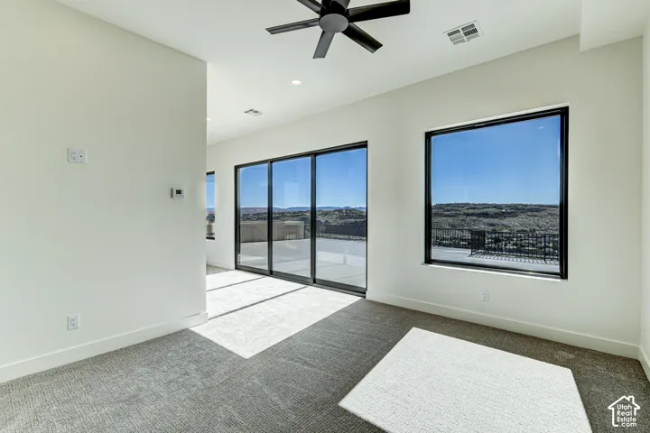 Interior space featuring neutral wall tones, wall-to-wall carpeting, black-framed windows, a multi-panel sliding glass door, and a ceiling-mounted matte black fan