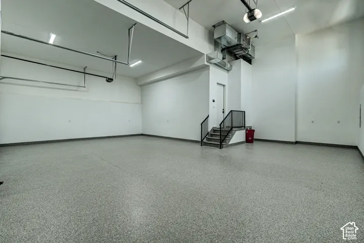 Spacious multi-car garage featuring high ceilings, speckled epoxy flooring, integrated LED lighting, and an internal staircase with a black metal railing