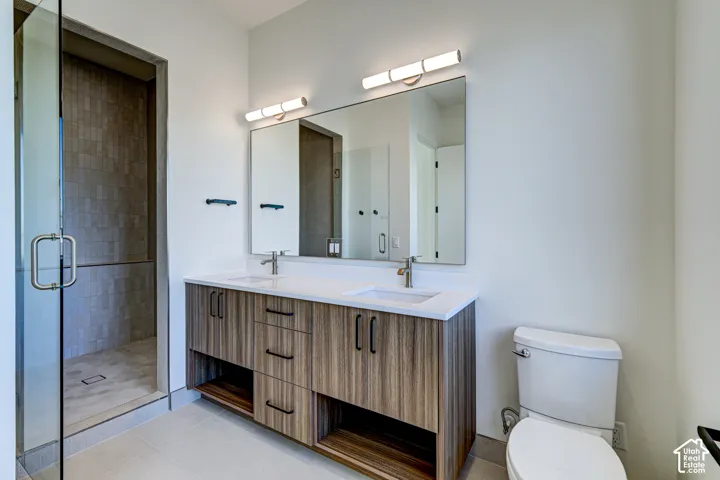 Dual-sink vanity with wood-finish cabinetry, quartz countertop, large frameless mirror, glass-enclosed shower with tile surround, and dual wall-mounted light fixtures