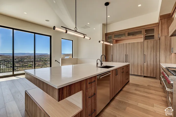 Kitchen featuring wood-finish cabinetry, an oversized island with a stone-surface countertop, recessed ceiling lighting, linear pendant fixtures, and wood-finish flooring