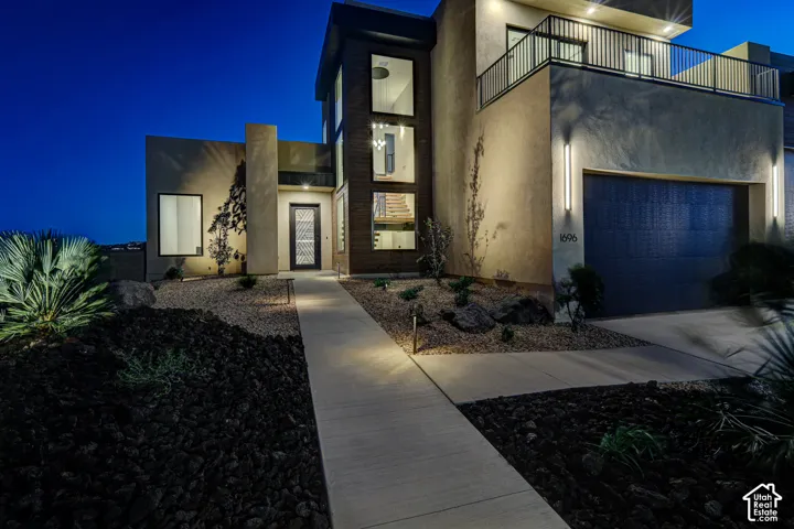 Modern multi-story exterior featuring smooth stucco siding, vertical wood-panel accents, expansive multi-pane windows, a gated second-level balcony with metal railing, and a concrete walkway