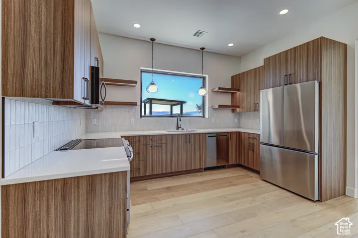 Kitchen featuring wood-grain cabinetry, quartz countertops, vertical tile backsplash, stainless steel appliances, and integrated pendant lighting