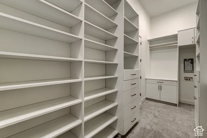 Custom walk-in storage featuring floor-to-ceiling white shelving, a five-drawer built-in cabinet, overhead hanging rods, and neutral carpeting