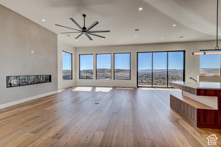 Open floor plan featuring wood-finish flooring, recessed lighting, a linear built-in fireplace, a ceiling fan with multiple blades, and large windows with mountain scenery