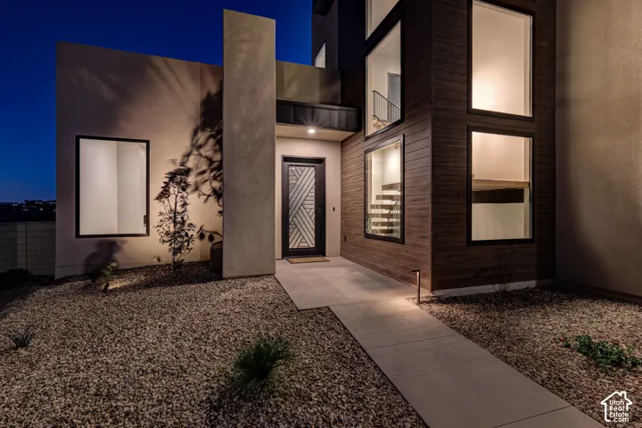 Contemporary architectural exterior featuring smooth stucco siding, wood-finish paneling, large-format glass windows, and a geometric-patterned metal entry door