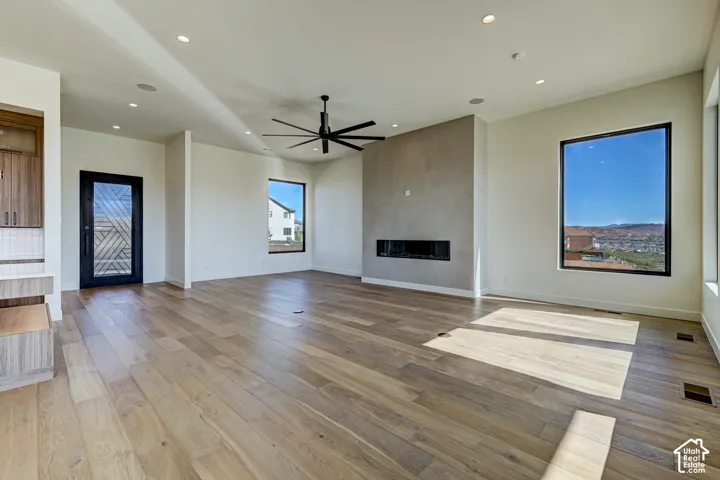 Living area featuring wood-finish flooring, a linear fireplace with a textured surround, recessed lighting, a multi-blade ceiling fan, and black-framed windows