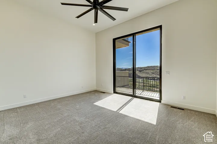 High-ceiling room featuring neutral carpeting, a black matte ceiling fan, and sliding glass doors opening to a private balcony with metal railing