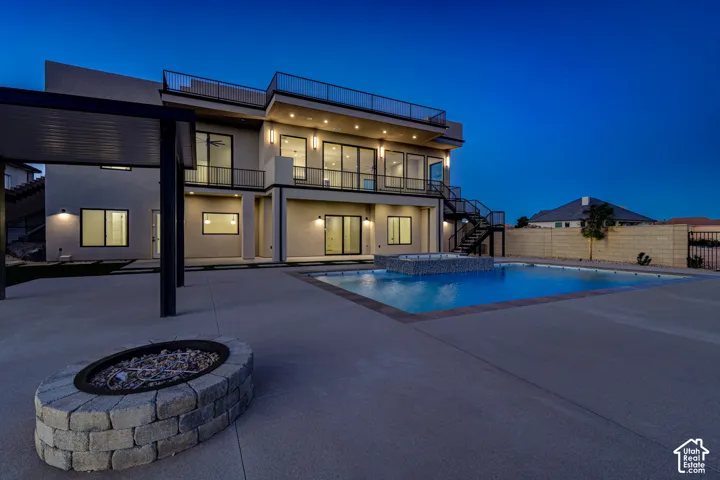 Exterior grounds featuring a multi-level concrete patio, a swimming pool with a stone-accented spa, a built-in circular stone fire pit, and a covered pergola
