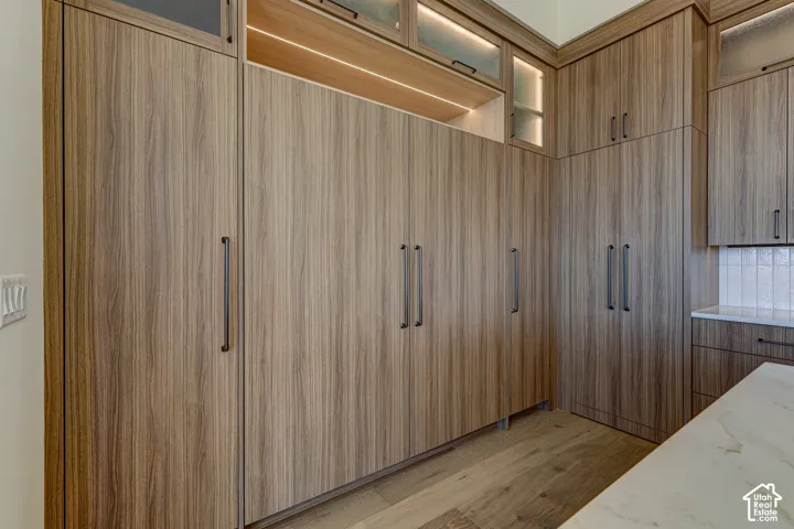 Floor-to-ceiling wood-finish cabinetry featuring integrated lighting, glass-front upper displays, matte black hardware, and stone-surface countertops
