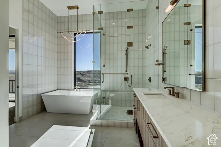 Freestanding soaking tub, walk-in glass-enclosed shower, dual-sink vanity with stone-finish countertop, linear geometric pendant lighting, and full-height wall tiling