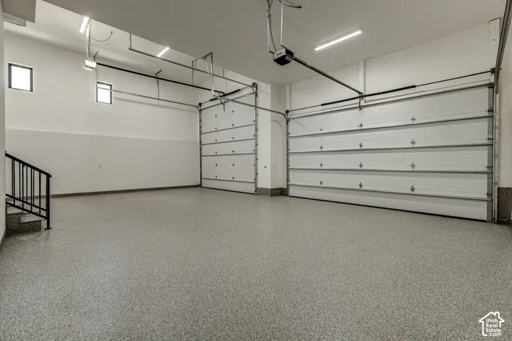 Spacious garage featuring an epoxy-coated floor, two high-clearance overhead doors, LED ceiling lighting, and black metal handrailing