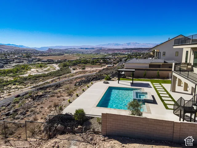 Multi-level rear terrace featuring a rectangular swimming pool, integrated spa, concrete deck, and pergola with mountain backdrop
