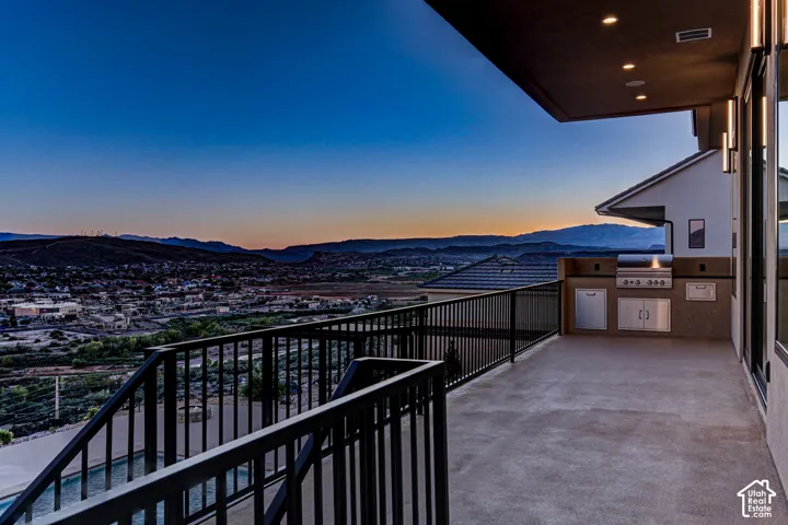 Covered balcony featuring an outdoor kitchen with stainless steel built-in grill and cabinetry, black metal railings, recessed ceiling lighting, and mountain, city, and river backdrop