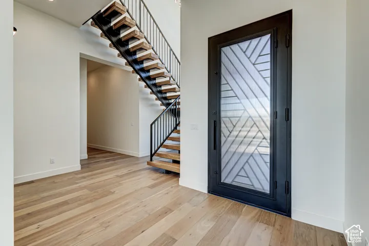 Entryway featuring a custom black metal door with geometric glass inlay, wood-finish flooring, and an open-riser staircase with wood treads and a black metal railing