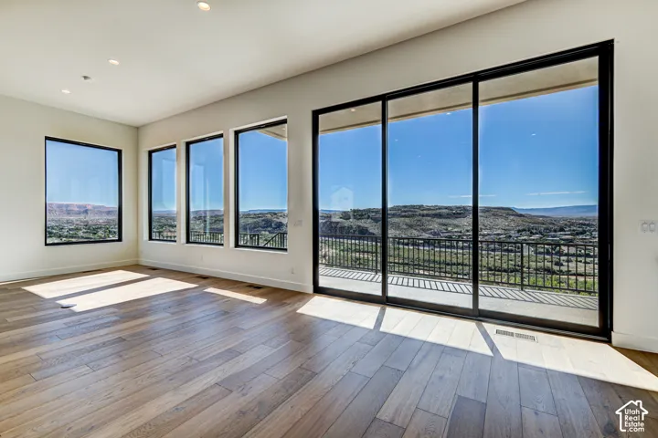 Large-format sliding glass doors, expansive picture windows, wood-finish flooring, recessed lighting, and metal balcony railing