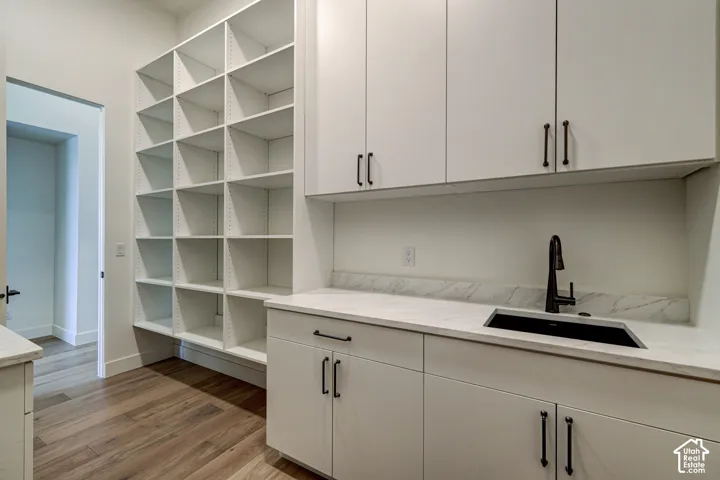 Custom cabinetry featuring expansive floor-to-ceiling open shelving, stone-composite countertops, integrated sink with matte black faucet, and wood-finish flooring