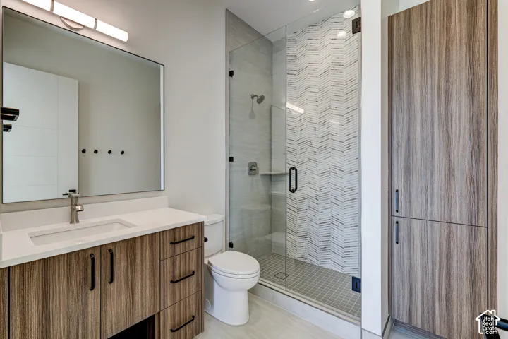 Wood-finish cabinetry, white countertop with an integrated sink, frameless glass shower enclosure featuring decorative tile accents, and matching floor-to-ceiling built-in storage