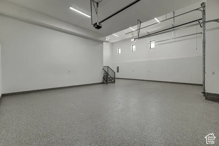 Expansive garage featuring high ceilings, speckled epoxy flooring, linear LED lighting, and a metal staircase with a black handrail
