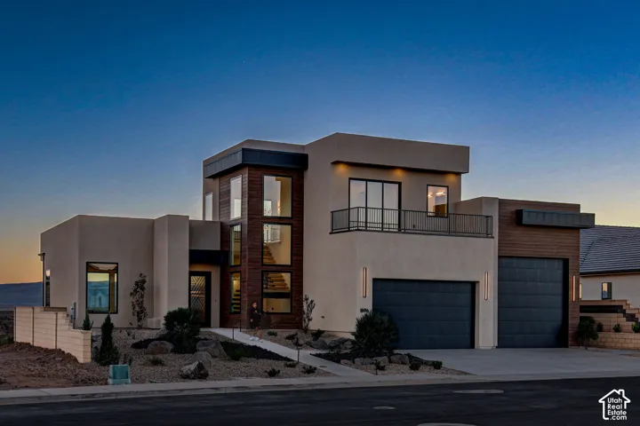 Contemporary multi-level exterior featuring smooth stucco finish, wood-paneled accent sections, floor-to-ceiling windows, second-story balcony with metal railing, and 4-car RV Garage