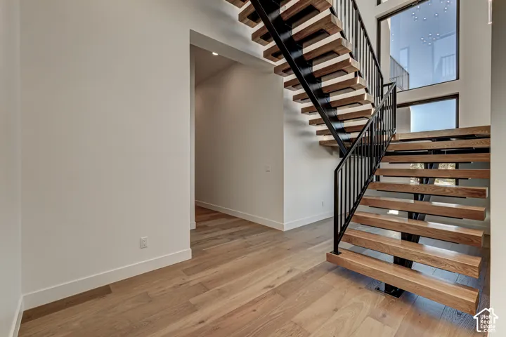 Floating staircase featuring open wood-finish treads, matte black metal stringers, and a vertical metal railing, complemented by wood-finish flooring and expansive multi-story windows