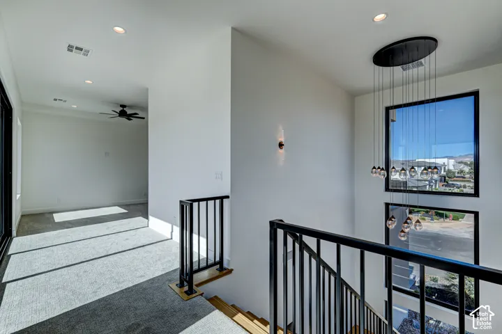 Multi-story staircase featuring matte black metal balusters, stacked floor-to-ceiling windows, a cascading modern pendant chandelier, recessed lighting, and carpeted flooring