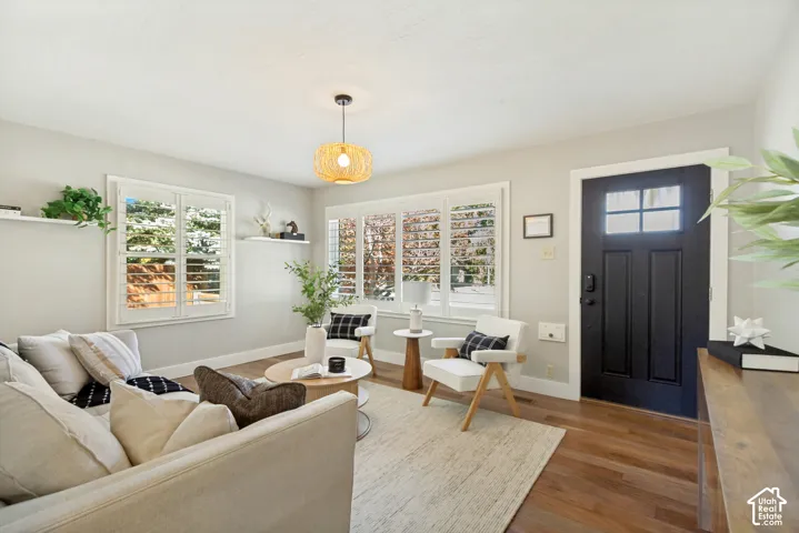 Living area featuring wood-finish flooring, white plantation shutters, a textured pendant light fixture, and a bold black exterior door with glass panes