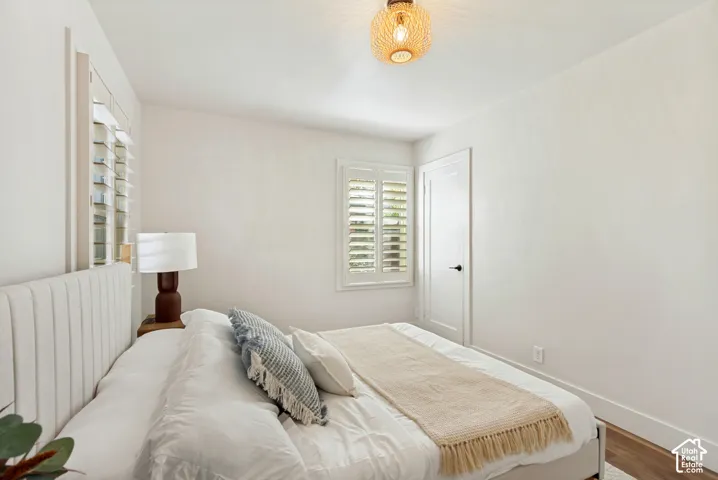 Room featuring neutral wall paint, wood-finish flooring, white plantation shutters, a solid-core interior door with matte black hardware, and a textured drum-style flush-mount light fixture