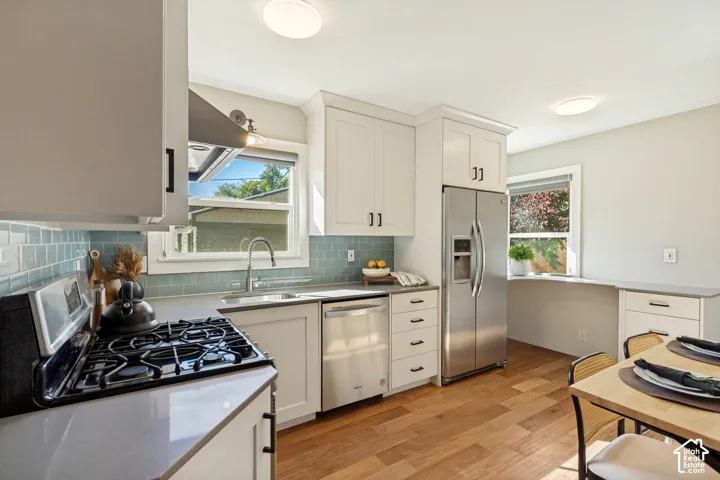 Kitchen featuring white shaker-style cabinetry, stainless steel appliances, blue subway tile backsplash, quartz countertops, and wood-finish flooring