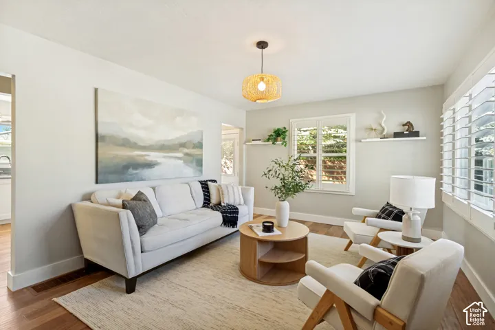 Living area featuring wood-finish flooring, plantation shutters, wall-mounted floating shelves, and a textured pendant light fixture