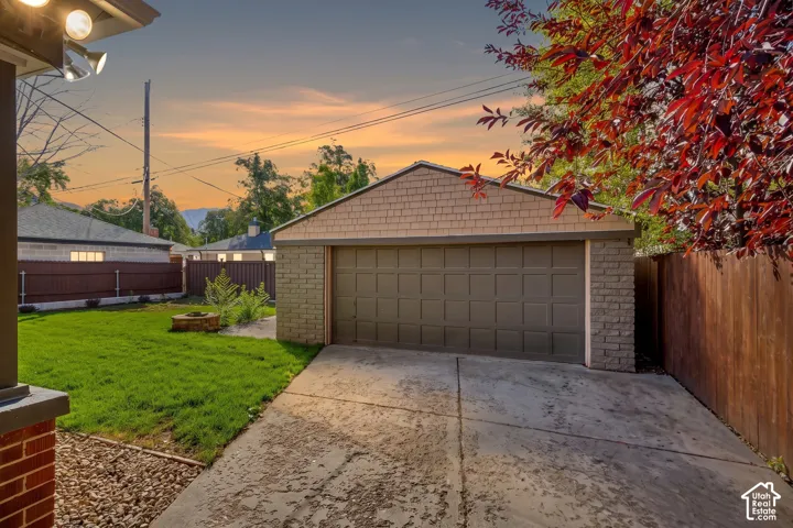 Detached garage featuring brick masonry, shingle siding, and a concrete driveway, complemented by a grass lawn, fire pit, and privacy fencing