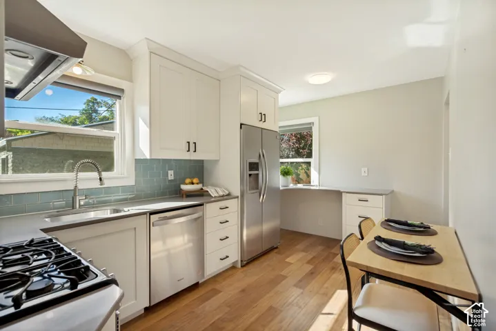 Kitchen featuring white shaker-style cabinetry, stainless steel appliances, blue subway tile backsplash, and wood-finish flooring