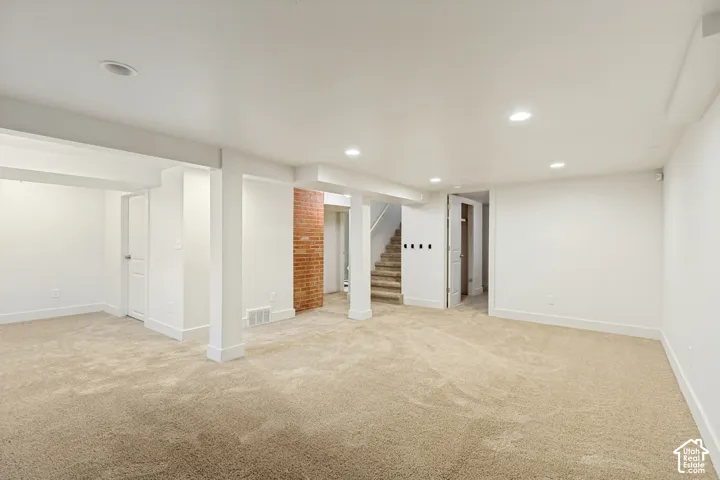 Open-concept interior featuring recessed lighting, exposed brick pillar, neutral wall-to-wall carpeting, and structural support columns