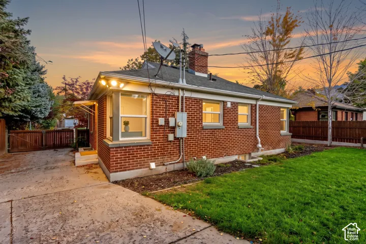 Red brick exterior featuring a chimney, concrete driveway, wood-paneled fence, and manicured lawn