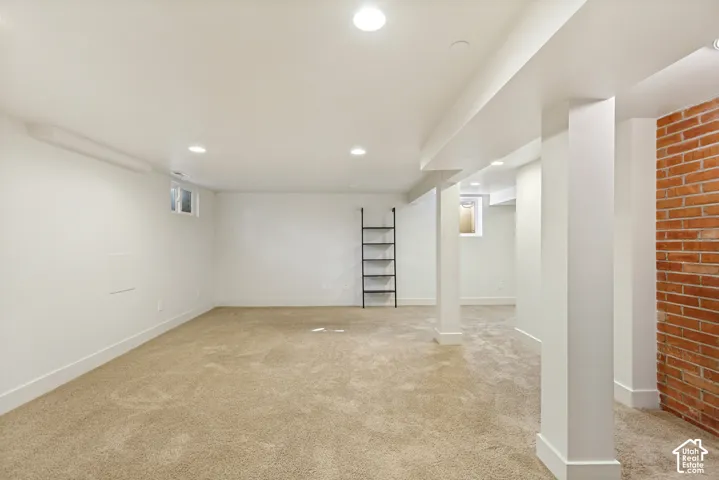 Open floor plan featuring wall-to-wall carpeting, recessed lighting, a structural red brick accent wall, and built-in metal shelving