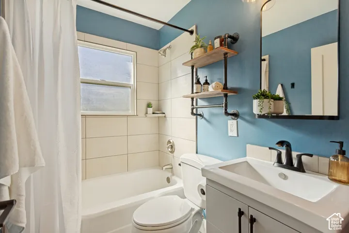 Bathroom featuring a vanity with a rectangular sink, matte black widespread faucet, tub with large-format tile surround, and wall-mounted industrial-style shelving