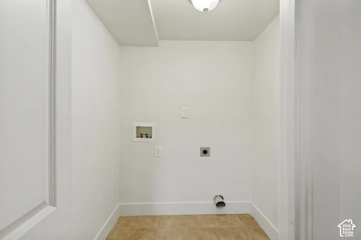 Dedicated utility area featuring tile flooring, neutral wall finishes, recessed water hookups, a standard electrical outlet, and an exhaust vent
