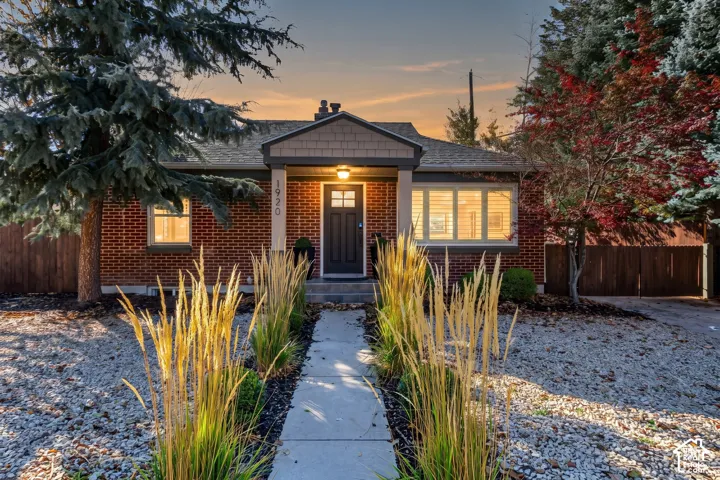 Red brick exterior with shingle-style gable detailing, covered front entryway, concrete walkway, and mature landscaping