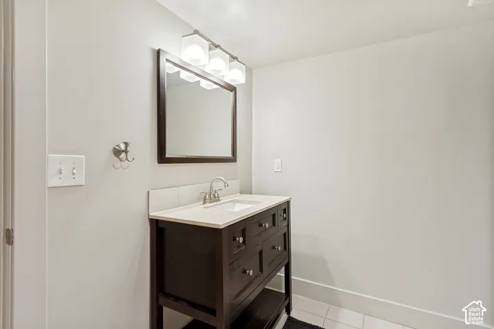 Dark wood vanity with a white countertop, integrated rectangular sink, three-light glass fixture, framed rectangular mirror, and satin nickel hardware