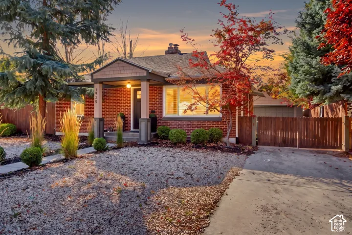 Brick exterior featuring a covered front porch with tapered columns, shake siding accents, and a concrete driveway leading to a detached garage