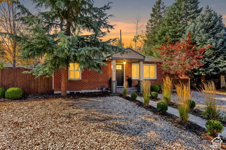 Brick exterior featuring a covered front porch, shake siding accents, mature evergreen trees, and low-maintenance rock landscaping