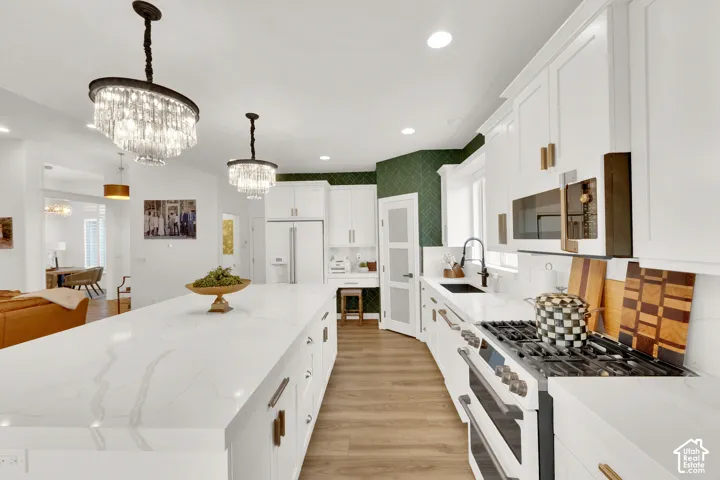 Kitchen featuring an oversized island with stone-finish countertops, shaker-style cabinetry, a six-burner gas range, dual crystal chandeliers, and wood-finish flooring